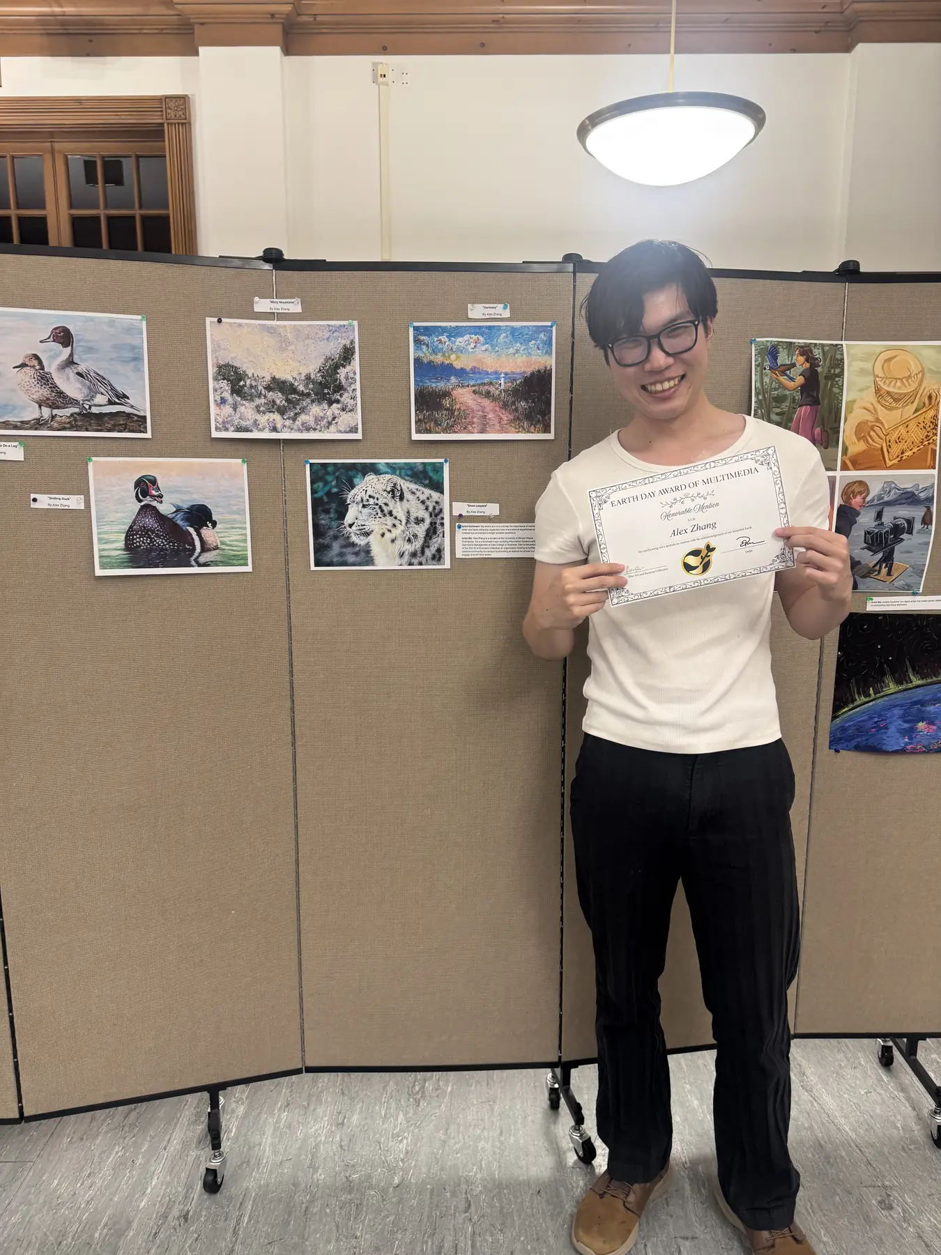 A student holding a certificate in front of a wall of student artwork