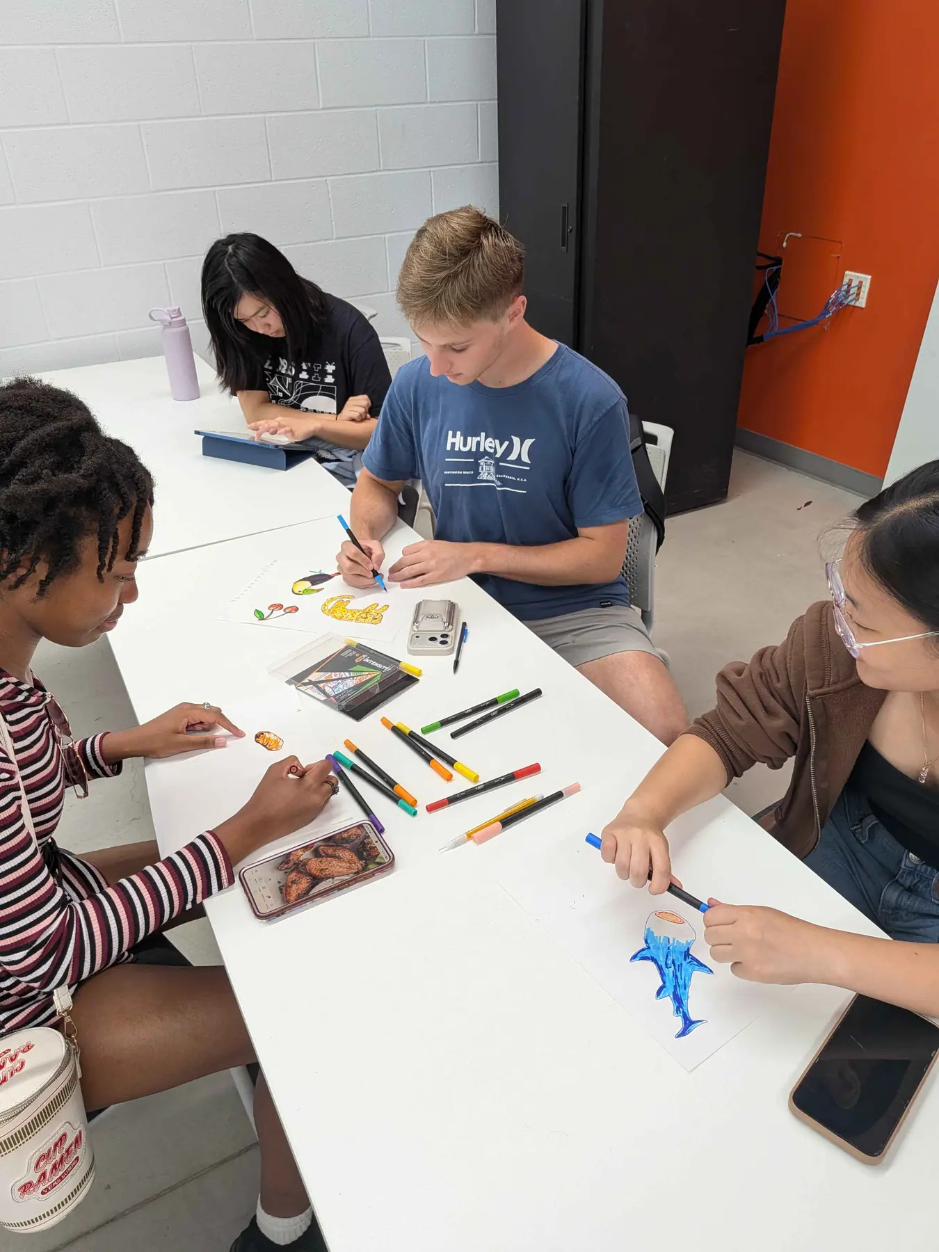 Students drawing together with markers around a long table